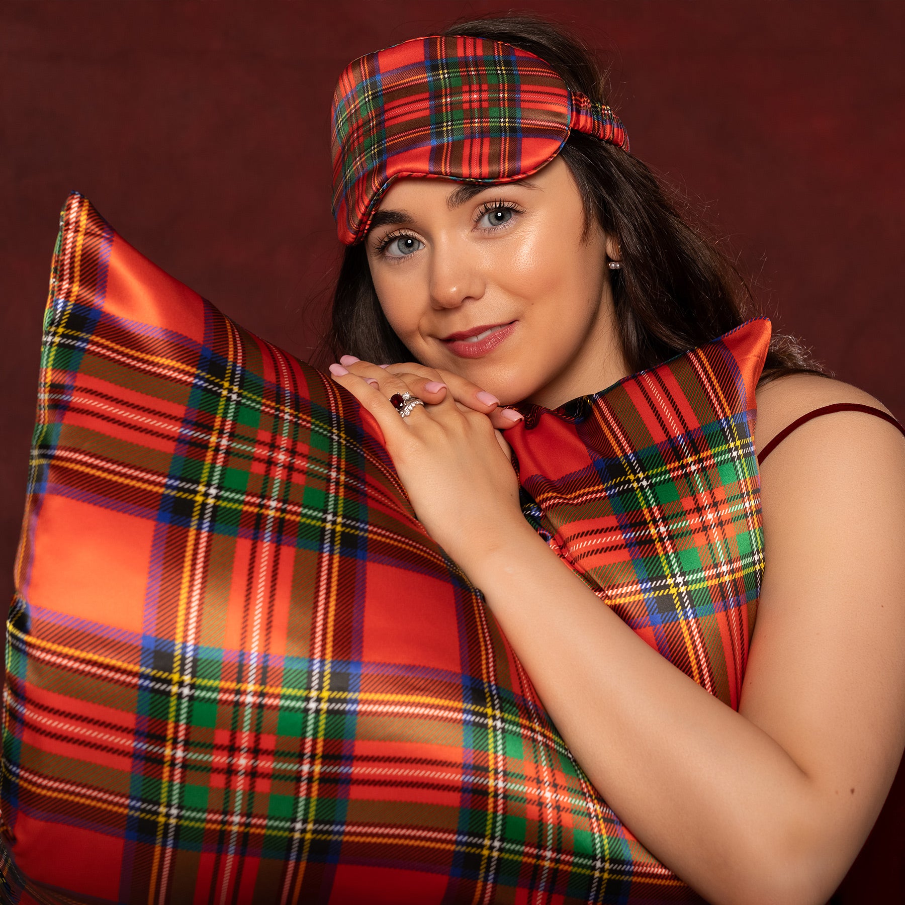 Woman wearing a red plaid silk eye mask and holding a matching Tartan red silk pillow