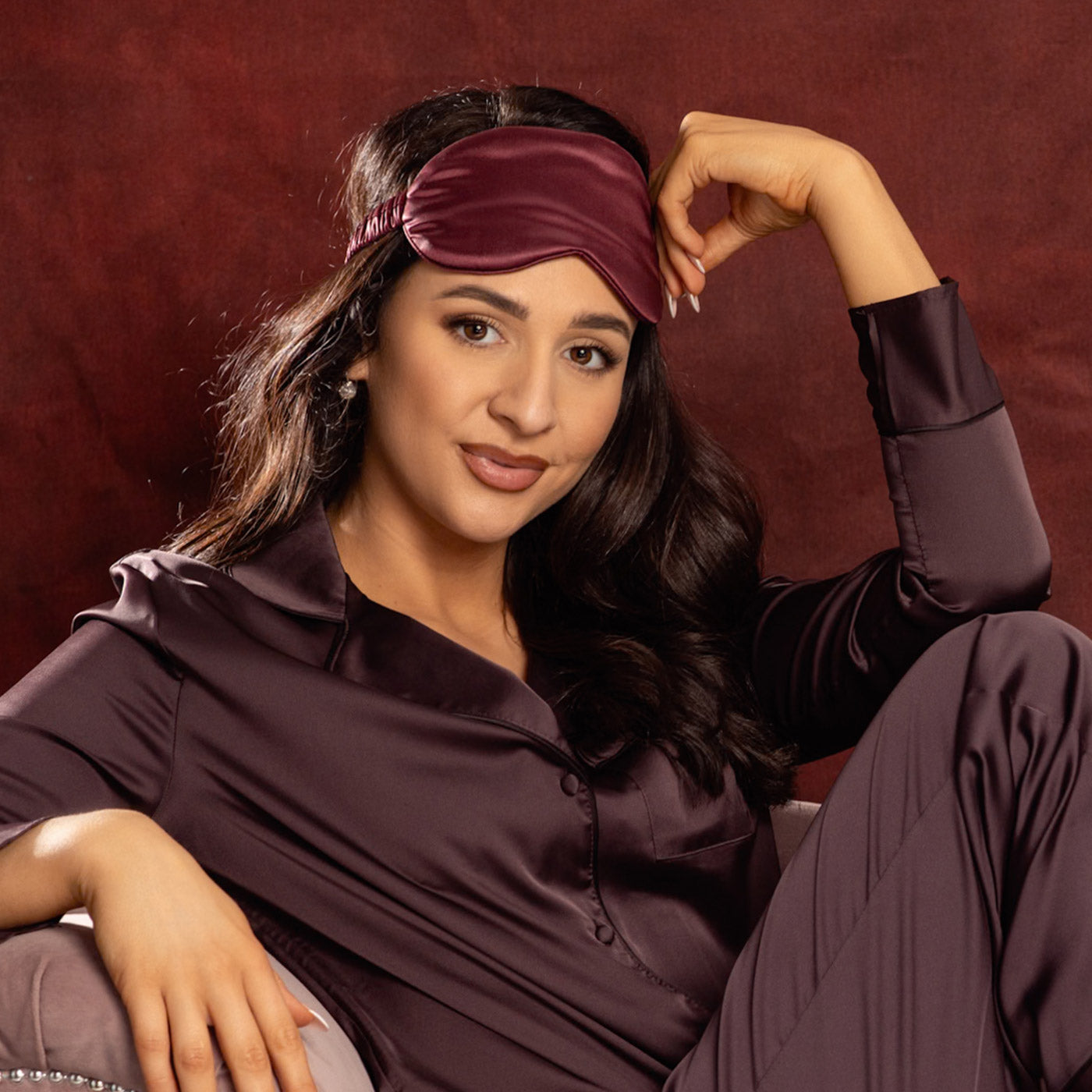 Woman wearing a burgundy  silk eye mask and robe against a red background