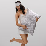 Woman holding a leopard silk pillow  and wearing a matching eye mask
