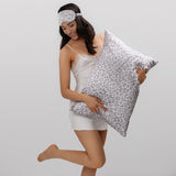 Woman holding a leopard silk pillow  and wearing a matching eye mask