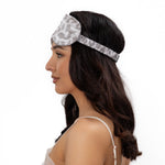 Woman wearing a silk leopard print sleep mask on a plain background