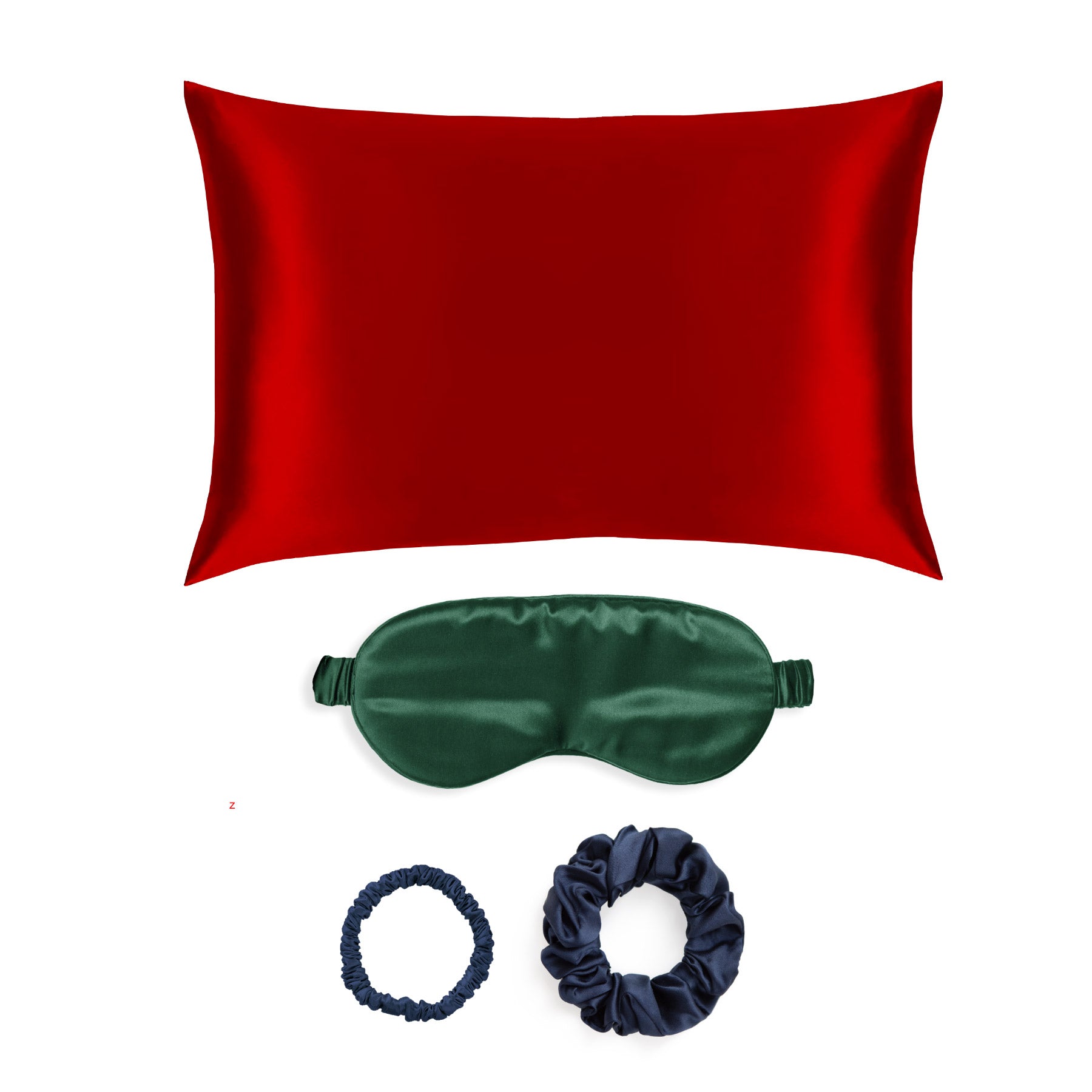 Red silk pillowcase, green sleep mask, and two navy scrunchies on a white background