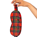Hand holding a red plaid eye mask against a white background